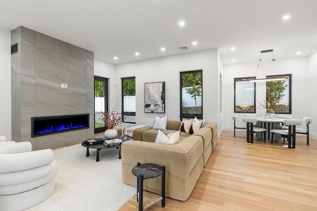 living area with light wood-style flooring, visible vents, a tiled fireplace, and recessed lighting