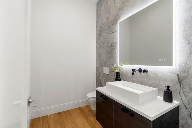 half bath with vanity, wood finished floors, toilet, and baseboards