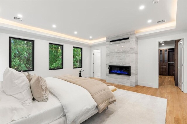 bedroom with light wood-style floors, visible vents, a raised ceiling, and a tile fireplace