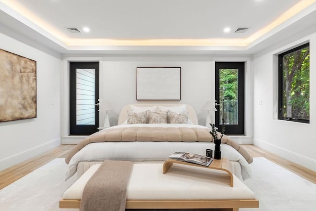 bedroom featuring a tray ceiling, wood finished floors, and visible vents