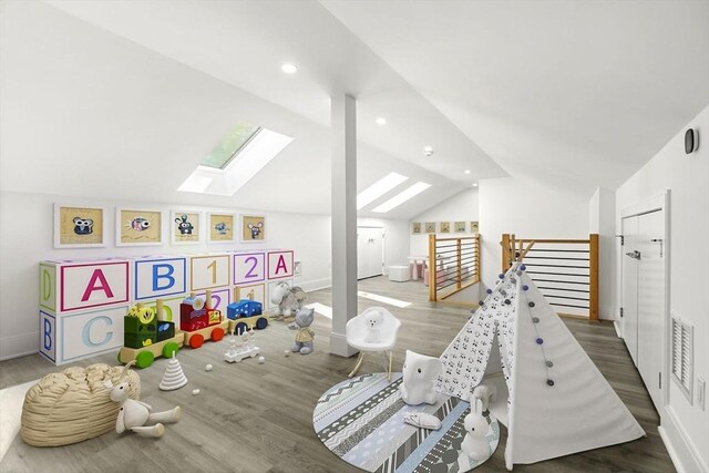 playroom with lofted ceiling with skylight, visible vents, and wood finished floors