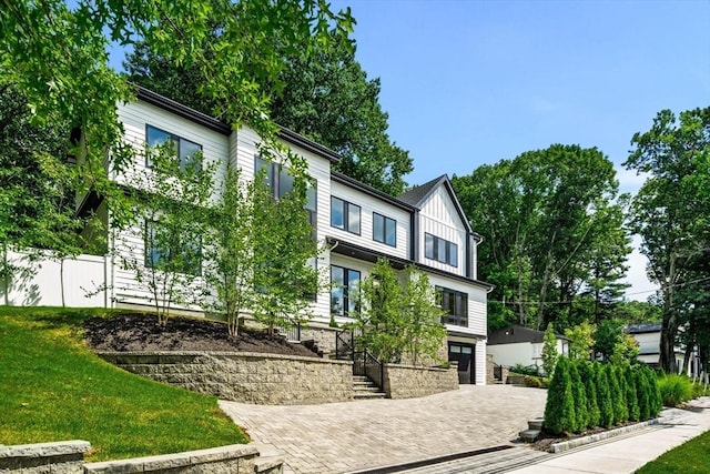 view of front facade featuring board and batten siding, fence, a front lawn, and decorative driveway