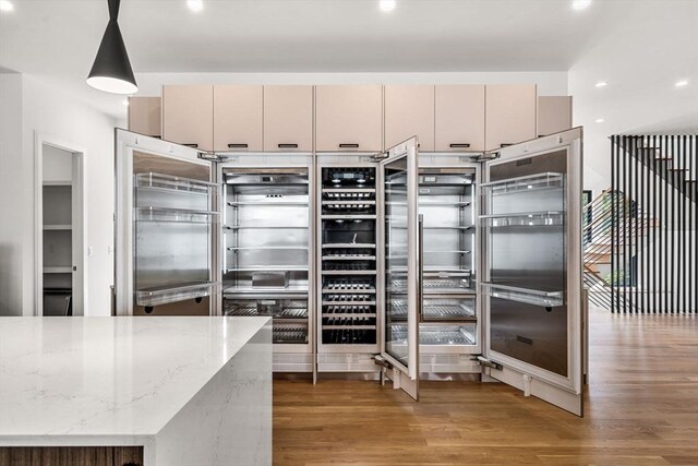 kitchen with light stone countertops, cream cabinetry, wood finished floors, and decorative light fixtures