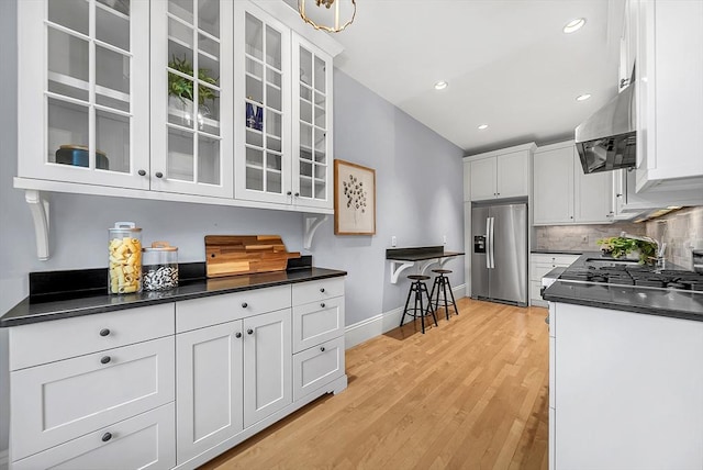 318 Commonwealth Ave Unit 3, Boston, MA 02115 - kitchen featuring stainless steel refrigerator with ice dispenser, dark countertops, white cabinetry, wall chimney range hood, and backsplash