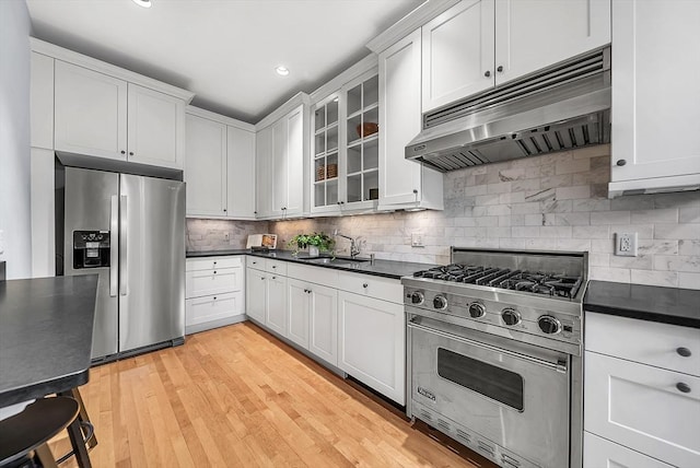 318 Commonwealth Ave Unit 3, Boston, MA 02115 - kitchen featuring appliances with stainless steel finishes, under cabinet range hood, dark countertops, glass insert cabinets, and decorative backsplash