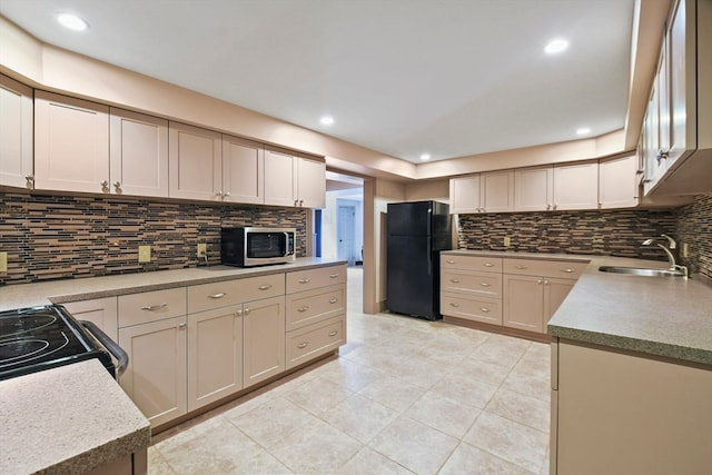 kitchen with cream cabinetry, sink, black appliances, light tile patterned floors, and tasteful backsplash