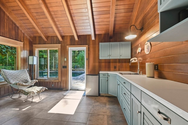 interior space with vaulted ceiling with beams, dark tile patterned flooring, wooden walls, wooden ceiling, and sink