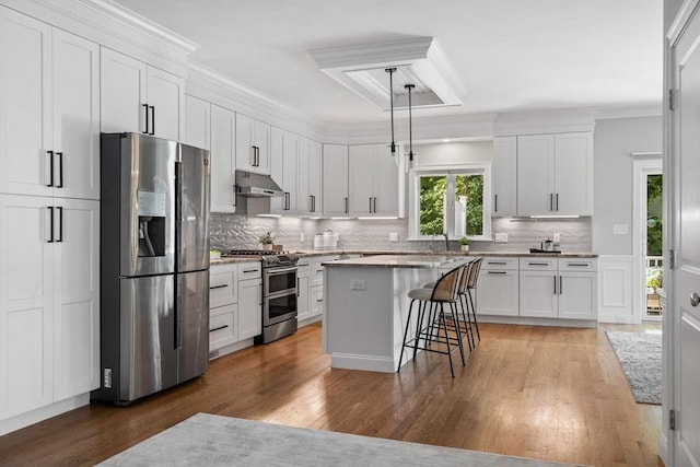 125 Ash St Unit 1, Waltham, MA 02453 - kitchen with stainless steel appliances, under cabinet range hood, white cabinetry, a breakfast bar, and decorative backsplash