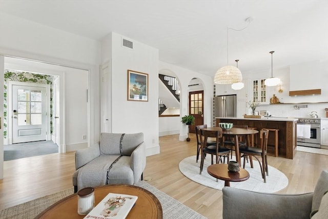 living room featuring stairway, baseboards, visible vents, and light wood finished floors