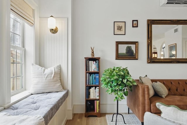 sitting room with a wall unit AC, visible vents, and wood finished floors