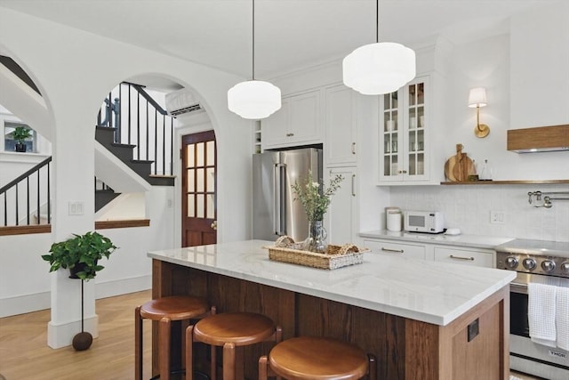 kitchen featuring a breakfast bar area, stainless steel appliances, white cabinets, a center island, and glass insert cabinets