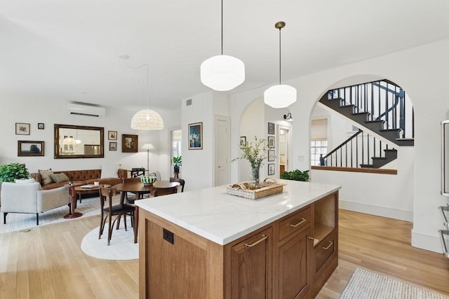 kitchen with arched walkways, pendant lighting, light wood-style floors, an AC wall unit, and a kitchen island