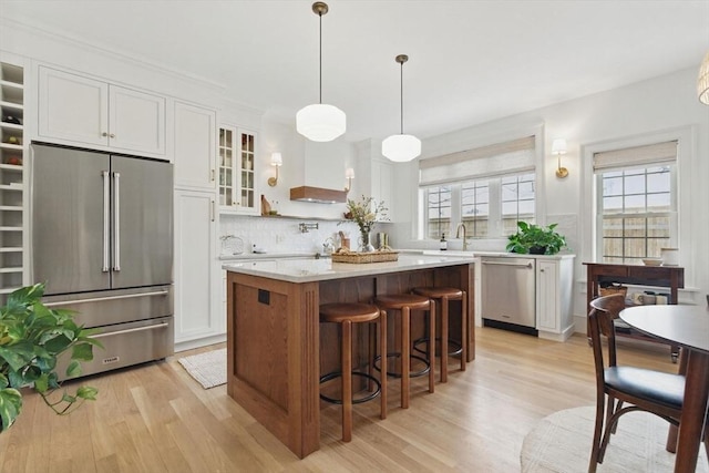 kitchen with white cabinetry, appliances with stainless steel finishes, light wood-type flooring, a center island, and glass insert cabinets