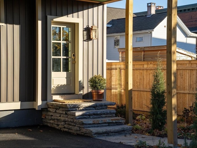 view of exterior entry with board and batten siding and fence