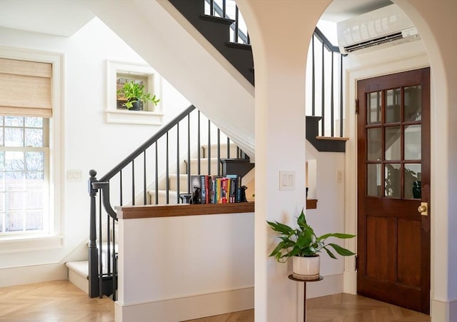 staircase with arched walkways, a wall unit AC, and a wealth of natural light