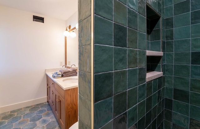 bathroom featuring baseboards, visible vents, tiled shower, stone finish floor, and vanity