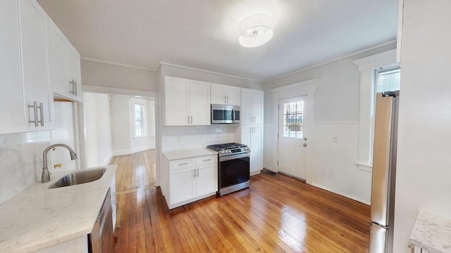 kitchen with white cabinetry, sink, tasteful backsplash, light hardwood / wood-style flooring, and appliances with stainless steel finishes