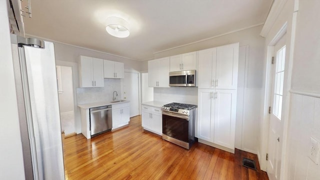 kitchen featuring white cabinets, decorative backsplash, light wood-type flooring, and stainless steel appliances