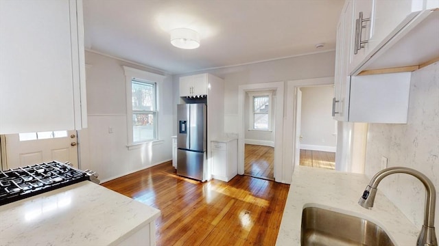 kitchen with light stone countertops, sink, stainless steel refrigerator with ice dispenser, wood-type flooring, and white cabinets