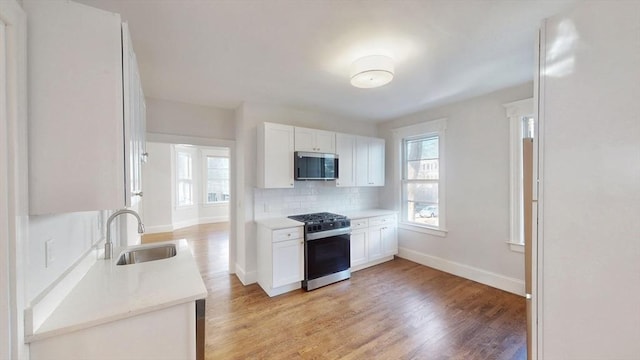 kitchen with decorative backsplash, appliances with stainless steel finishes, sink, white cabinets, and light hardwood / wood-style floors