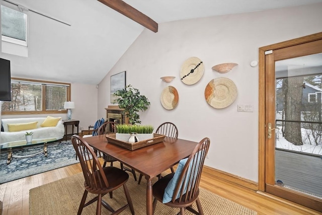 dining room with light wood-type flooring, a fireplace, and vaulted ceiling with beams