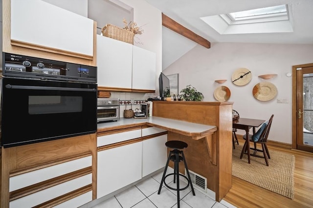 kitchen featuring black oven, lofted ceiling with skylight, light countertops, and white cabinets