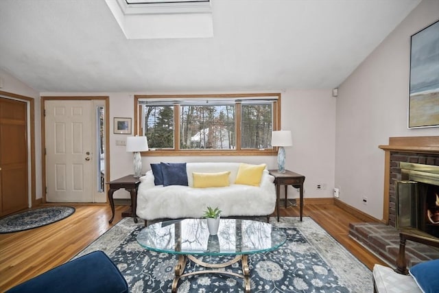 living area with a brick fireplace, vaulted ceiling with skylight, and wood finished floors