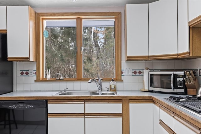 kitchen featuring tasteful backsplash, white cabinets, light countertops, black appliances, and a sink