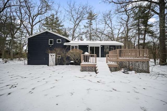 snow covered back of property with a garage and a wooden deck