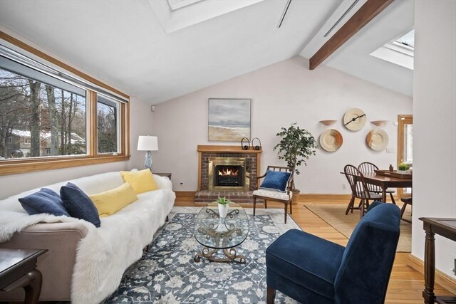 living room featuring a brick fireplace, baseboards, lofted ceiling with skylight, and light wood-style floors