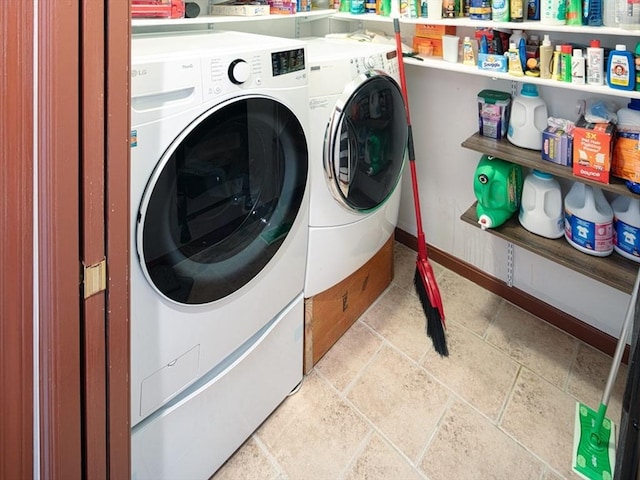 laundry area featuring laundry area, washing machine and clothes dryer, stone tile flooring, and baseboards