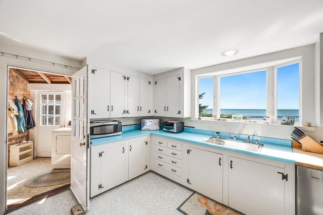 kitchen with a sink, white cabinetry, light countertops, appliances with stainless steel finishes, and washer / dryer