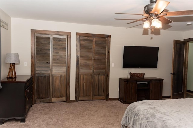 bedroom featuring light carpet, ceiling fan, and two closets