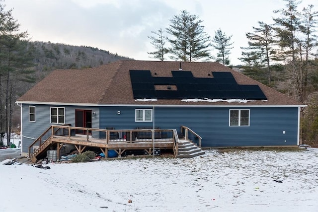 snow covered rear of property featuring a deck and solar panels