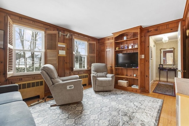 living room featuring light wood-type flooring, wooden walls, radiator heating unit, and ornamental molding