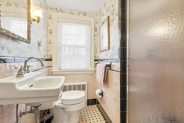 bathroom with toilet, a shower with shower door, sink, tile walls, and radiator heating unit