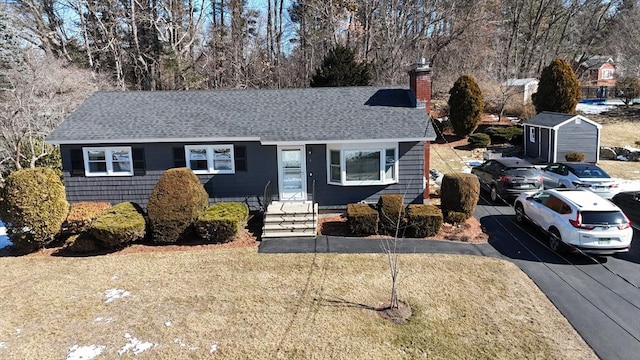 ranch-style house with a front yard, a chimney, and a shingled roof