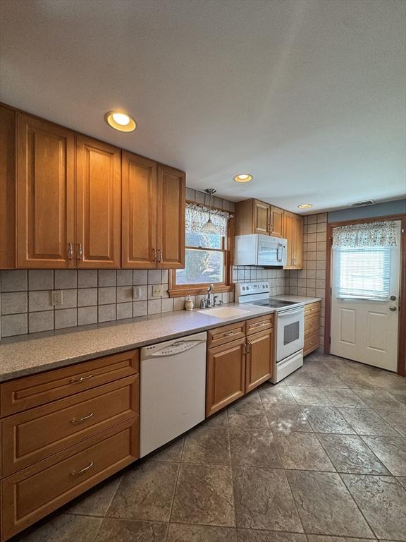 kitchen featuring brown cabinets, a sink, tasteful backsplash, white appliances, and light countertops