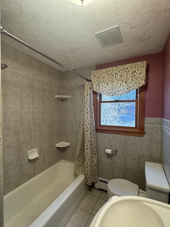 full bathroom with visible vents, a baseboard heating unit, toilet, tile patterned floors, and a textured ceiling