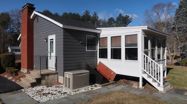 exterior space with a shingled roof, a sunroom, and a chimney