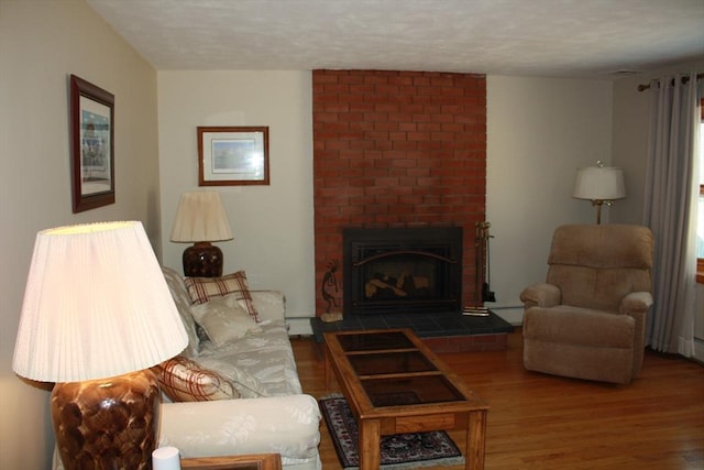 living area with a brick fireplace, a textured ceiling, and wood finished floors