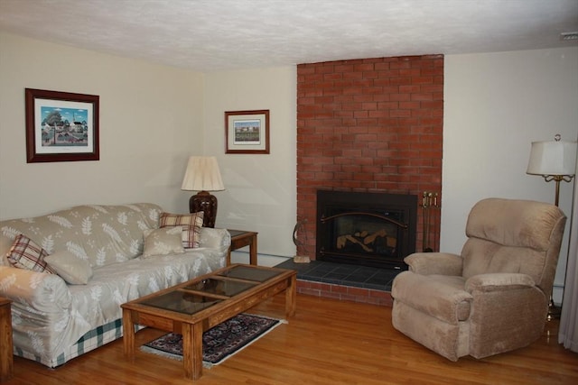 living area featuring a baseboard radiator, a textured ceiling, a brick fireplace, and wood finished floors