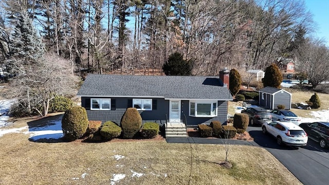 ranch-style house with a shingled roof, a front yard, an outbuilding, and a chimney