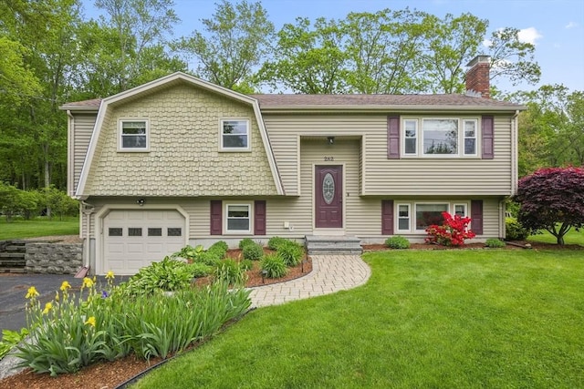 split foyer home with an attached garage, a chimney, driveway, and a front yard
