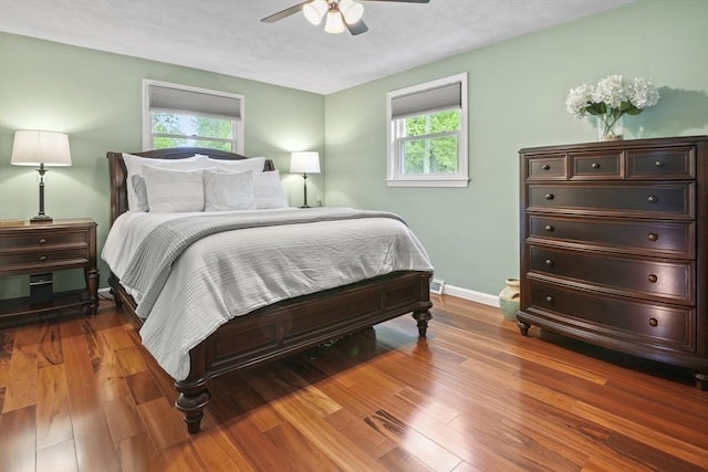 bedroom with multiple windows, wood-type flooring, baseboards, and a ceiling fan