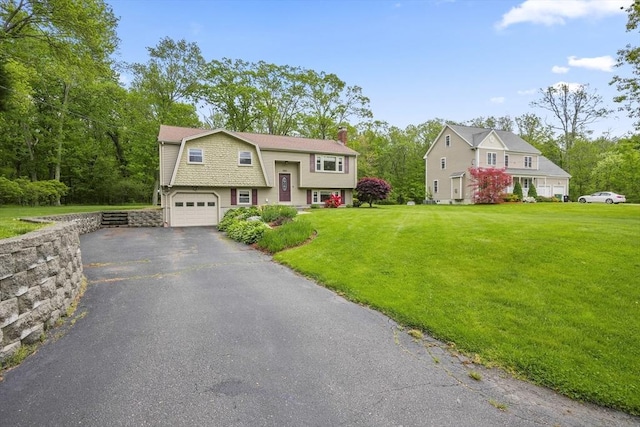 view of front of home with a gambrel roof, an attached garage, a chimney, asphalt driveway, and a front yard