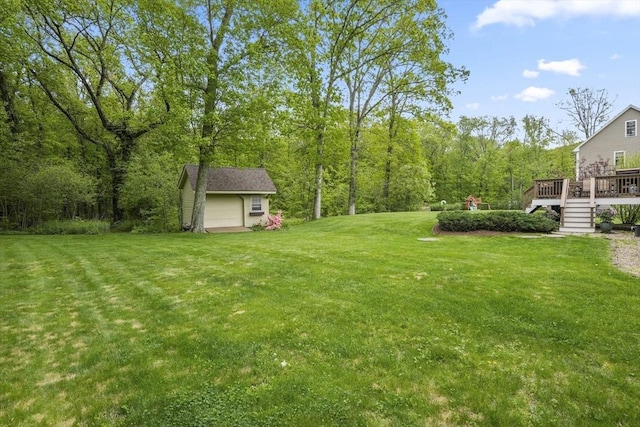 view of green lawn featuring a wooden deck, a garage, and an outbuilding
