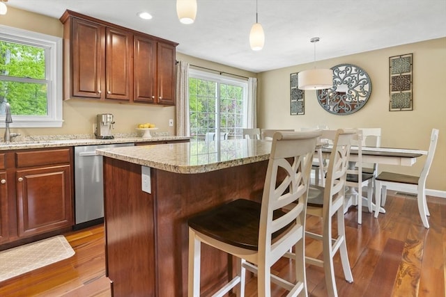 kitchen featuring dishwasher, wood finished floors, a breakfast bar, a sink, and hanging light fixtures