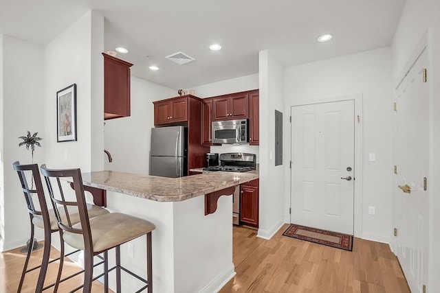 kitchen featuring a kitchen breakfast bar, light hardwood / wood-style floors, kitchen peninsula, and appliances with stainless steel finishes