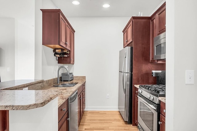 kitchen with sink, light hardwood / wood-style flooring, stainless steel appliances, light stone countertops, and kitchen peninsula